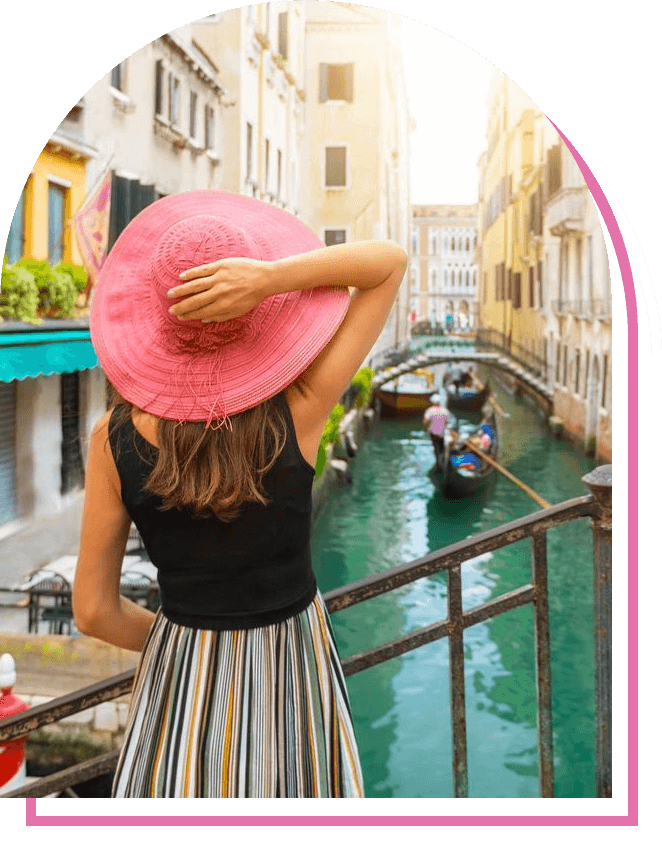 A woman in a pink hat standing on the side of a canal.